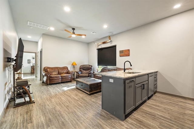 kitchen featuring light stone counters, ceiling fan, sink, hardwood / wood-style flooring, and gray cabinets