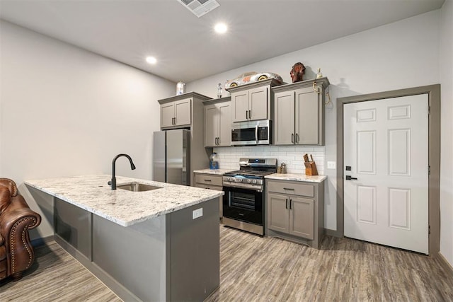 kitchen with gray cabinetry, sink, light stone countertops, appliances with stainless steel finishes, and light hardwood / wood-style floors