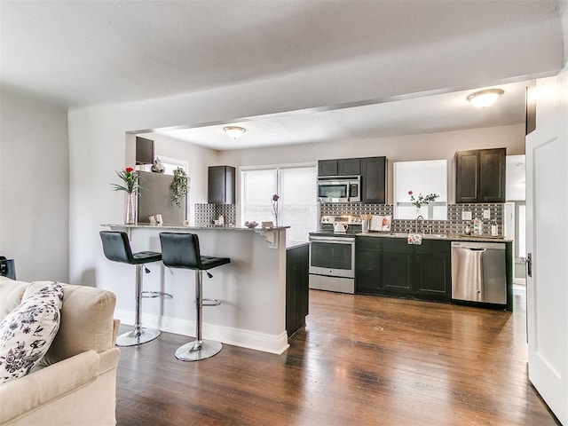 kitchen with a kitchen bar, tasteful backsplash, dark brown cabinetry, stainless steel appliances, and dark wood-type flooring