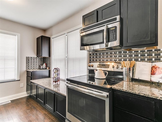 kitchen with stone countertops, dark hardwood / wood-style flooring, stainless steel appliances, and tasteful backsplash