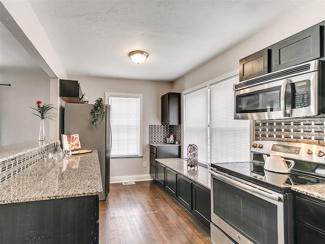 kitchen featuring decorative backsplash, light stone counters, dark hardwood / wood-style floors, and appliances with stainless steel finishes