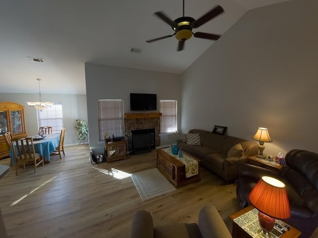 living room featuring ceiling fan with notable chandelier, a tiled fireplace, lofted ceiling, and light hardwood / wood-style flooring