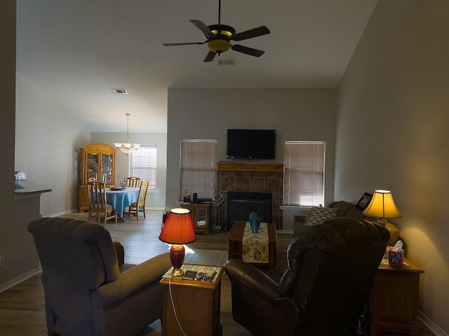 living room with a tile fireplace, wood-type flooring, and ceiling fan with notable chandelier