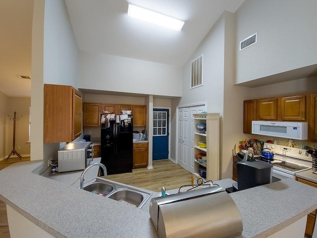 kitchen featuring white appliances, high vaulted ceiling, sink, light hardwood / wood-style flooring, and kitchen peninsula