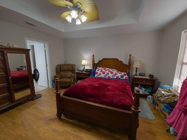 bedroom with ceiling fan, a raised ceiling, and light wood-type flooring