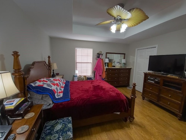 bedroom featuring light wood-type flooring, a raised ceiling, and ceiling fan