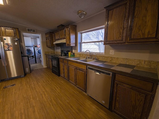 kitchen featuring appliances with stainless steel finishes, a textured ceiling, sink, washing machine and clothes dryer, and light hardwood / wood-style floors