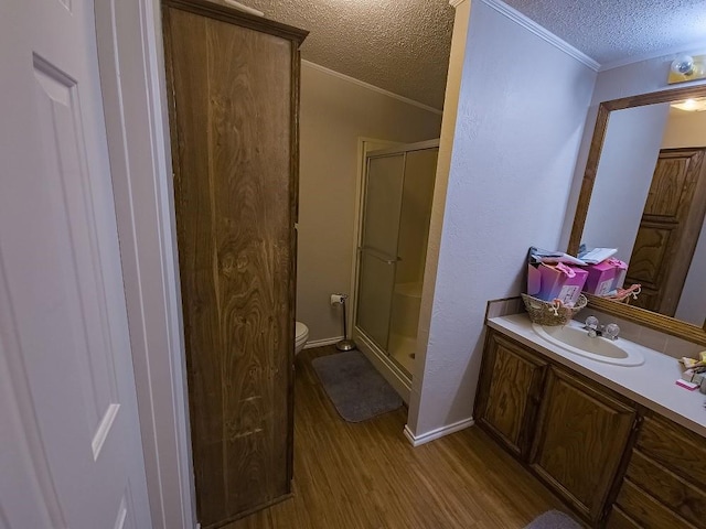 bathroom with vanity, wood-type flooring, crown molding, a textured ceiling, and a shower with shower door