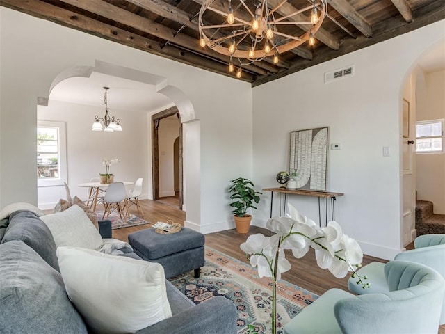 living room featuring beamed ceiling, a wealth of natural light, hardwood / wood-style floors, and a chandelier