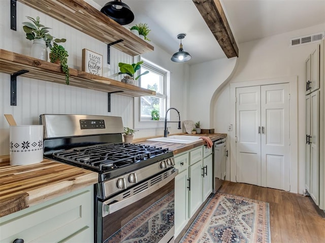 kitchen with sink, butcher block counters, beam ceiling, stainless steel appliances, and decorative light fixtures