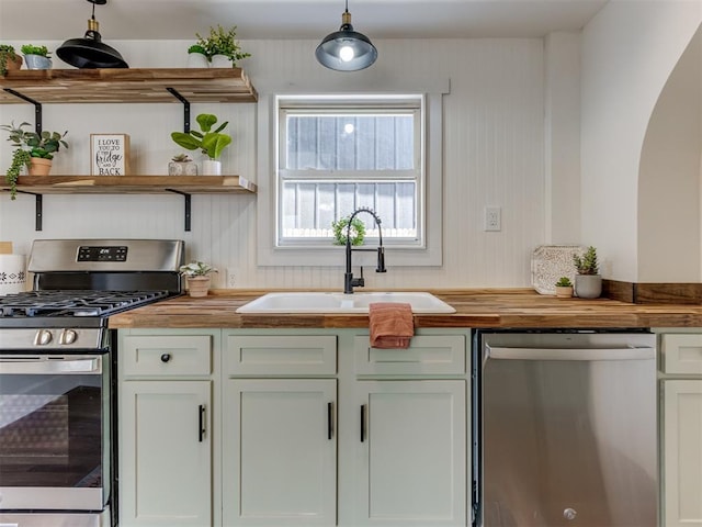 kitchen with appliances with stainless steel finishes, butcher block countertops, decorative light fixtures, sink, and white cabinets