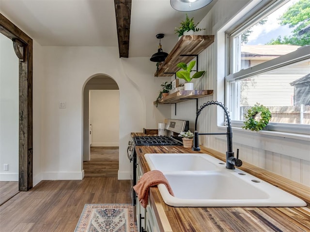 kitchen with beamed ceiling, sink, wooden counters, gas range, and light hardwood / wood-style flooring