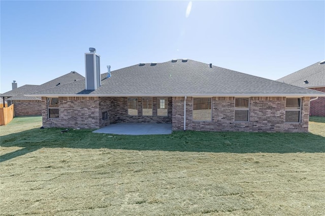 rear view of property featuring a shingled roof, a patio, a chimney, a yard, and brick siding