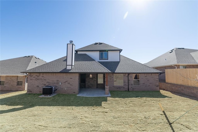 rear view of property featuring a yard, brick siding, a patio, and roof with shingles