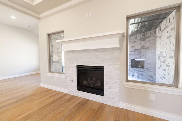 unfurnished living room with crown molding, baseboards, wood finished floors, and a stone fireplace