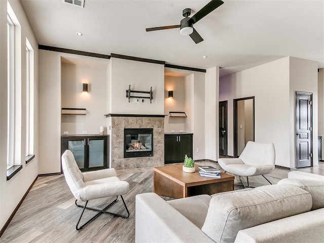 living room with hardwood / wood-style floors, ceiling fan, and a tiled fireplace