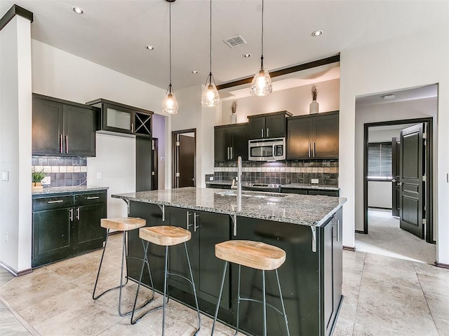 kitchen with pendant lighting, decorative backsplash, sink, and a kitchen island with sink