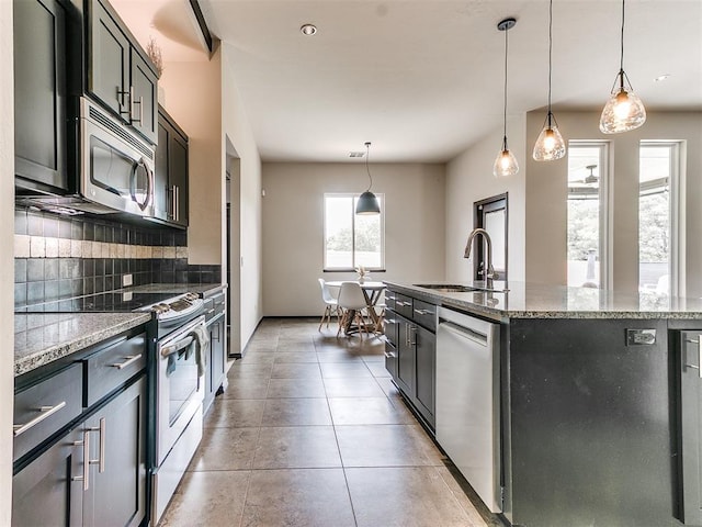 kitchen with pendant lighting, stainless steel appliances, a kitchen island with sink, and sink