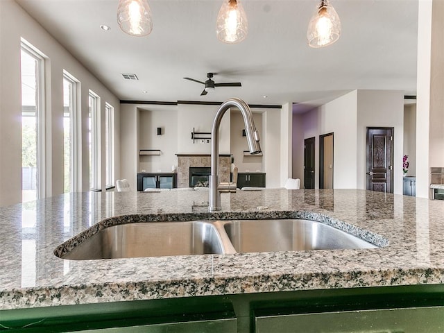 kitchen with a tile fireplace, light stone countertops, hanging light fixtures, and sink