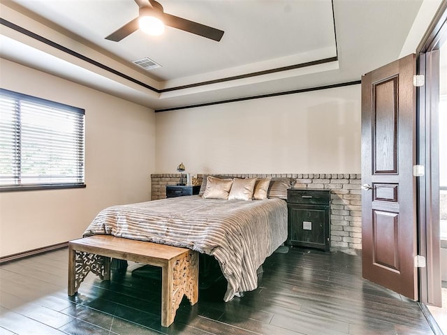 bedroom featuring dark hardwood / wood-style flooring, a tray ceiling, a wood stove, and ceiling fan