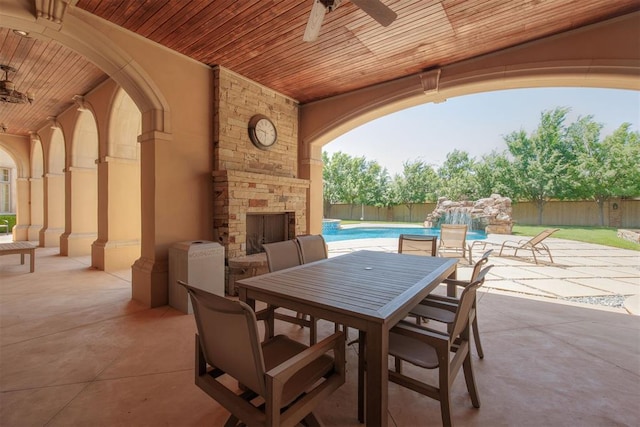 view of patio / terrace with an outdoor stone fireplace, ceiling fan, and a fenced in pool