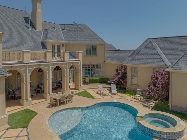 rear view of property featuring a swimming pool with hot tub, a balcony, and a patio area