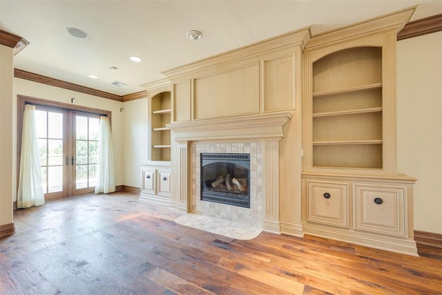 unfurnished living room featuring a tiled fireplace, wood-type flooring, ornamental molding, and french doors