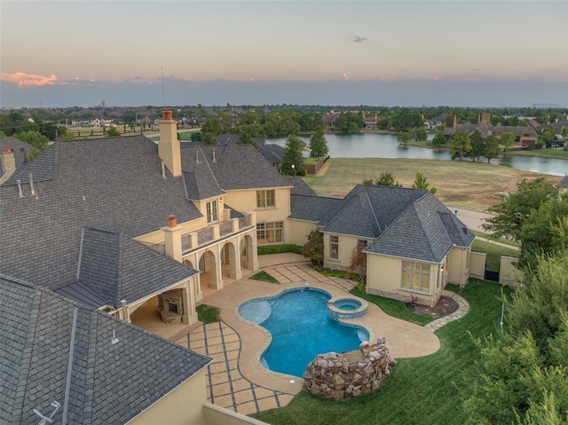 pool at dusk featuring an in ground hot tub, a patio, and a water view