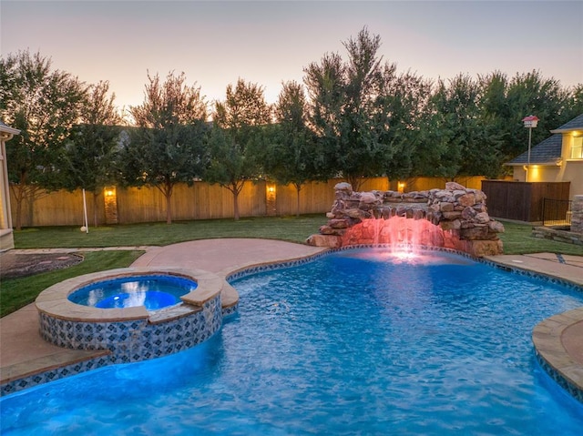 pool at dusk featuring a lawn, an in ground hot tub, and pool water feature