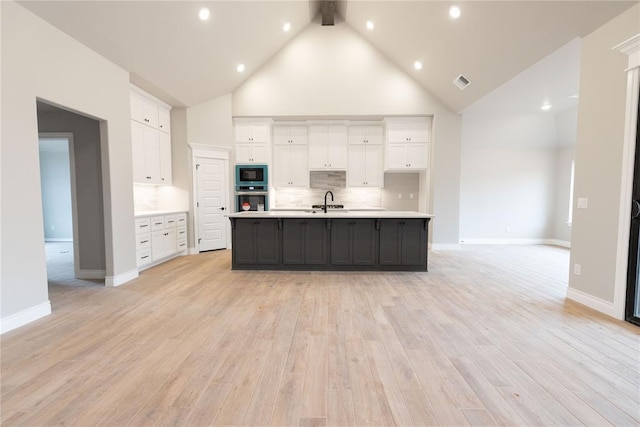 kitchen with light countertops, visible vents, white cabinets, stainless steel oven, and a sink