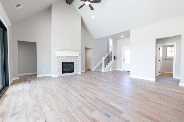 unfurnished living room with visible vents, ceiling fan, a fireplace, light wood finished floors, and high vaulted ceiling