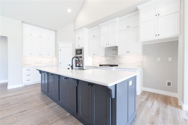 kitchen with light wood-style floors, stainless steel microwave, white cabinetry, and vaulted ceiling