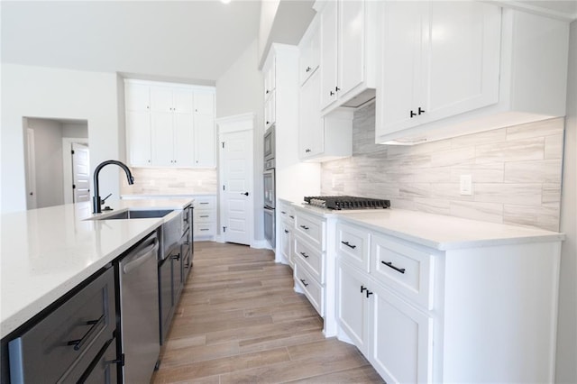 kitchen featuring light wood-style flooring, white cabinetry, appliances with stainless steel finishes, a sink, and backsplash