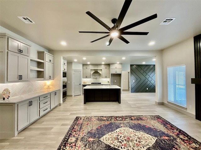 kitchen featuring tasteful backsplash, ceiling fan, wall chimney range hood, light hardwood / wood-style floors, and a kitchen island