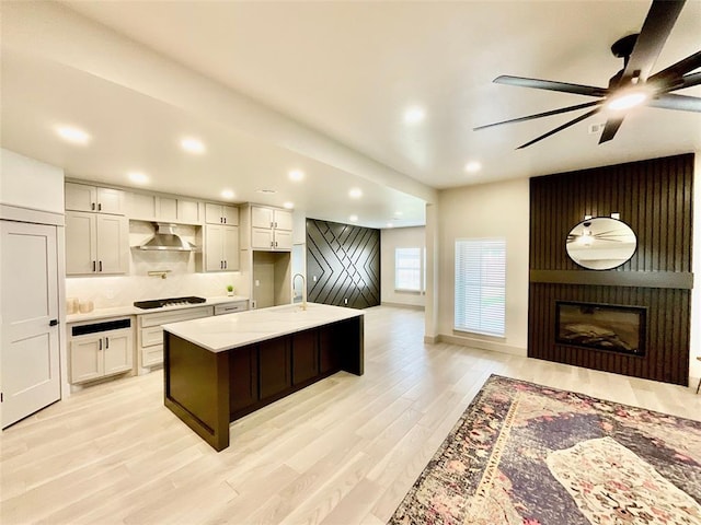 kitchen with gas stovetop, a fireplace, light hardwood / wood-style floors, white cabinetry, and an island with sink