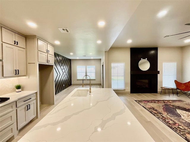 kitchen with white cabinets, sink, light hardwood / wood-style flooring, light stone countertops, and a fireplace