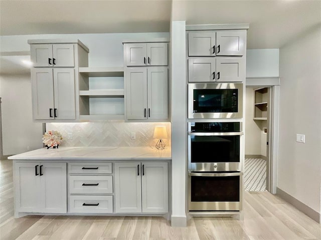 kitchen with decorative backsplash, light stone counters, light wood-type flooring, and stainless steel appliances