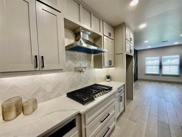 kitchen with tasteful backsplash, light stone counters, extractor fan, stainless steel gas stovetop, and light wood-type flooring