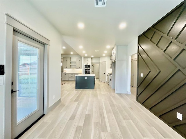 kitchen with light wood-type flooring, stainless steel double oven, a center island, and white cabinetry