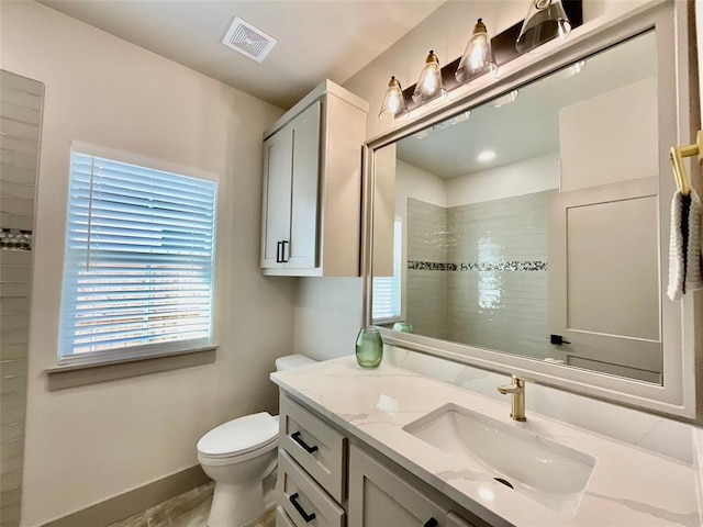 bathroom with tiled shower, vanity, and toilet