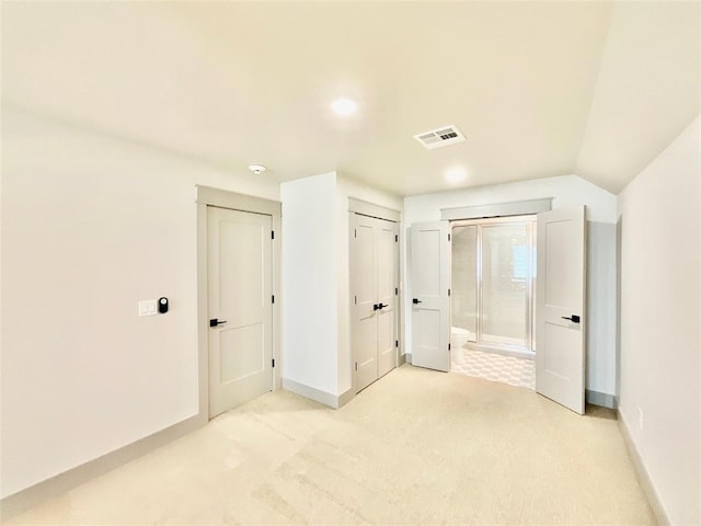 unfurnished bedroom with light colored carpet, lofted ceiling, and ensuite bathroom