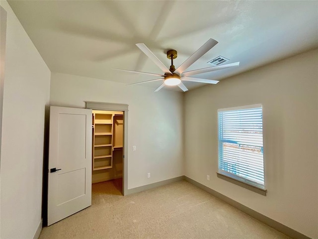 unfurnished bedroom featuring a closet, a spacious closet, ceiling fan, and light colored carpet