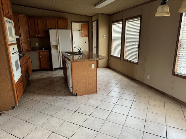 kitchen with sink, vaulted ceiling, decorative light fixtures, white appliances, and a kitchen island with sink