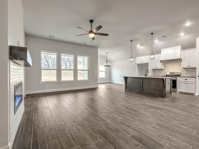 kitchen featuring an island with sink, white cabinets, hanging light fixtures, dark wood-type flooring, and stainless steel range oven