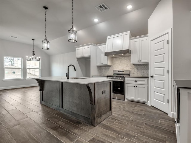 kitchen with pendant lighting, sink, stainless steel gas stove, white cabinets, and a center island with sink