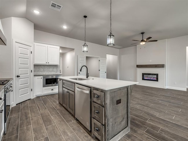 kitchen with appliances with stainless steel finishes, tasteful backsplash, sink, white cabinets, and a center island with sink