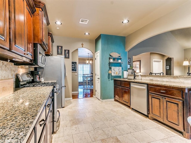 kitchen with sink, stainless steel appliances, light stone counters, a notable chandelier, and decorative backsplash