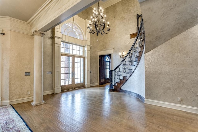 foyer entrance featuring french doors, ornate columns, wood-type flooring, a chandelier, and ornamental molding