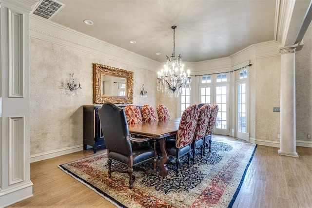 dining area featuring hardwood / wood-style flooring, a notable chandelier, crown molding, and ornate columns