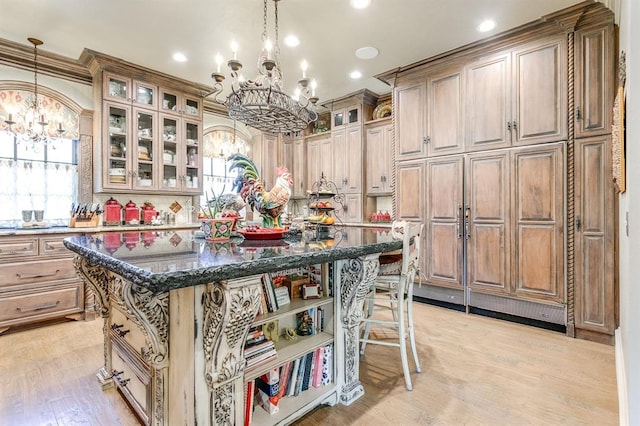 kitchen with decorative light fixtures, dark stone countertops, a kitchen breakfast bar, a kitchen island, and light hardwood / wood-style floors